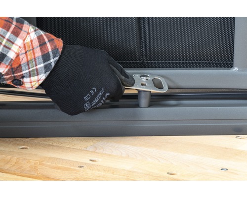 Une personne fixe un support métallique argenté sur une grille de fenêtre.