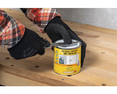 Une personne portant des gants ouvre une boîte de laque PU acrylique pour fenêtres et portes avec un outil de la marque Hornbach.