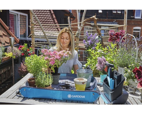 Une femme plante des fleurs sur un balcon avec un tapis de plantation, des fleurs, des pots et des outils de jardinage.