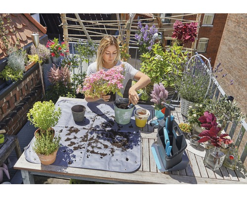 Une femme plante des fleurs sur un balcon avec une natte de plantation et des outils de jardinage
