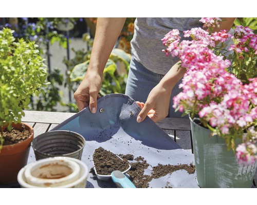 Une personne utilise un tapis de plantation pour rempoter des plantes à l''extérieur.