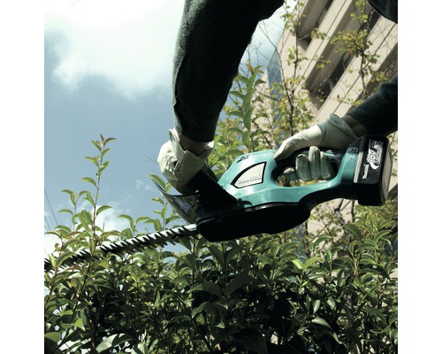Une personne taille une haie avec un taille-haie sans fil.