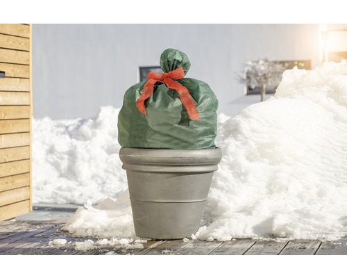 Pflanzkübel mit Winterschutzhaube und Schleife im verschneiten Garten