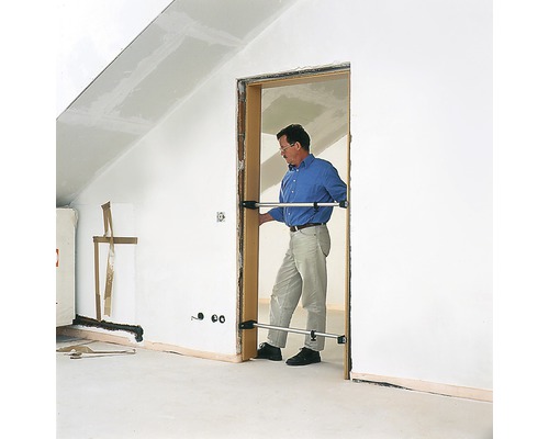 Un homme installe un dormant de porte avec des entretoises dans une pièce mansardée.