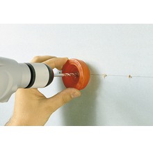 Eine Person bohrt mit einer Bohrmaschine und einem Staubschutzaufsatz in eine Wand.