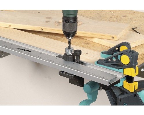 Eine Bohrmaschine mit Dübelbohrlehre beim Bohren in ein Holzbrett mit Wolfcraft Dübelzwingen.