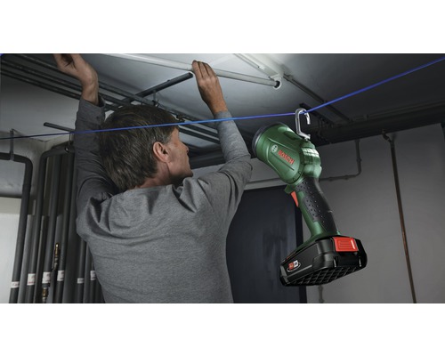 Un homme fixe une lampe de travail Bosch avec un crochet sur une corde dans une cave