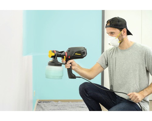 Un homme utilise un pistolet à peinture Wagner pour peindre un mur.