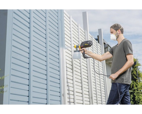 Un homme peint une clôture avec un pulvérisateur de peinture.