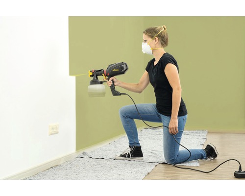 Une femme utilise un pistolet à peinture pour peindre un mur.