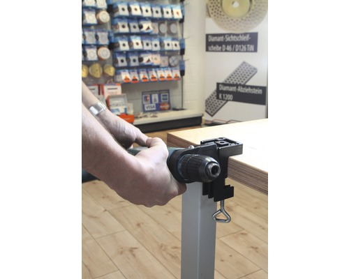 Un homme fixe une perceuse à une table avec un serre-table.