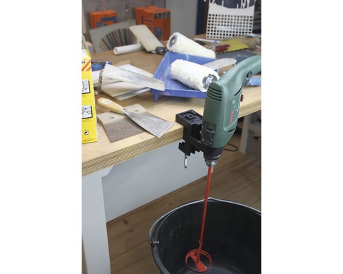 Un mélangeur de perceuse vert avec agitateur rouge dans un seau noir sur une table avec des outils.