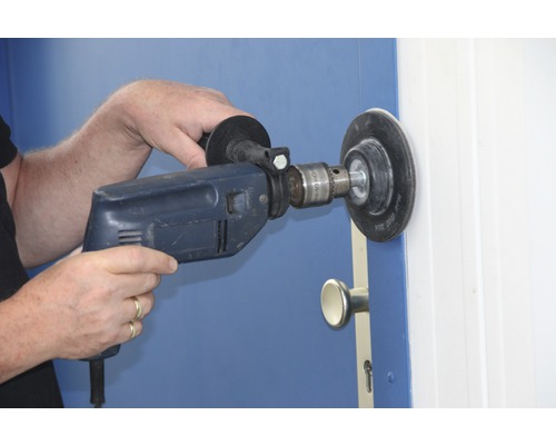 Eine Person verwendet eine Bohrmaschine mit Schleifscheibe an einer Tür.