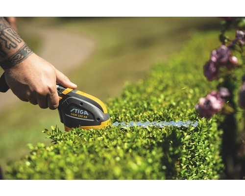 Stiga Logo. Person schneidet Hecke mit einer Akku-Grasschere.