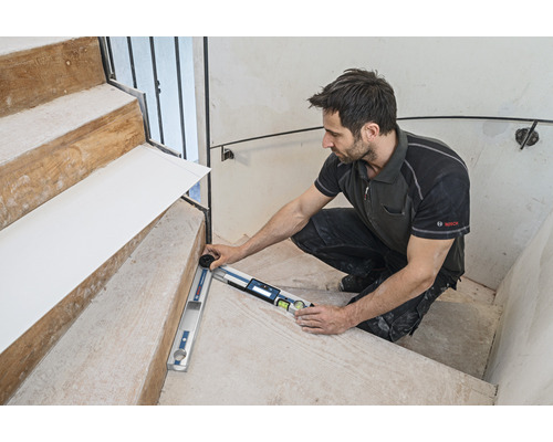 Un artisan mesure un escalier avec un rapporteur d'angle. Logo Bosch