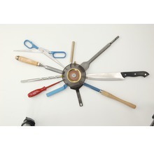 Disposition de divers outils autour d''une meule : ciseaux, burin, foret, tournevis, spatule, couteau et outil de tournage.