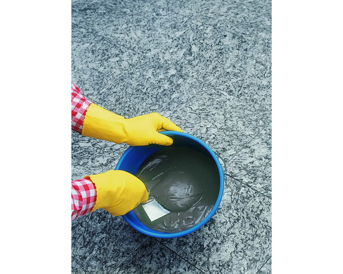 Une personne mélange de la colle à carrelage dans un seau à l''aide d''une spatule.