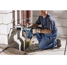 Ein Handwerker bohrt mit einem Bohrhammer ein Loch in eine Mauer, um Rohre zu befestigen.