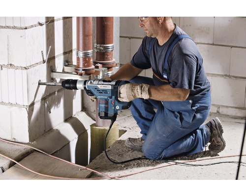 Ein Handwerker bohrt mit einem Bohrhammer ein Loch in eine Mauer, um Rohre zu befestigen.