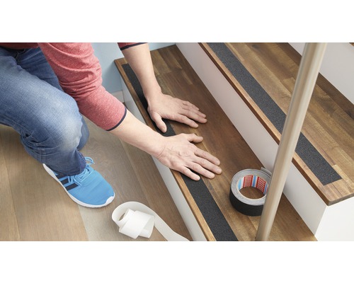 Personne fixant des bandes antidérapantes sur un escalier en bois.