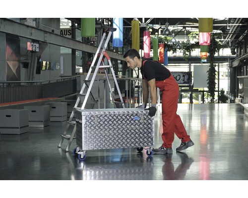 Mann schiebt Werkzeugkiste mit Rollen neben einer Leiter in einem Gebäude
