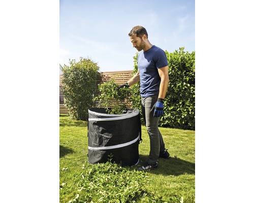 Un homme remplit un sac de jardin avec des déchets de jardin dans le jardin.