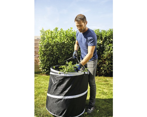 Aide de jardin : Un homme remplit un sac à feuilles de déchets de jardin dans le jardin.