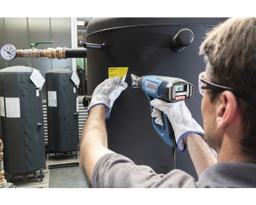 Eine Person entfernt mit einem Heissluftgebläse ein Etikett von einem Heizöltank.