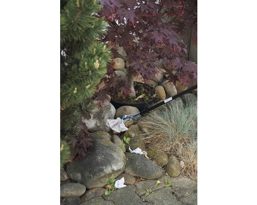 Scène avec une pince de ramassage des déchets ramassant du papier dans un jardin avec des pierres et des plantes