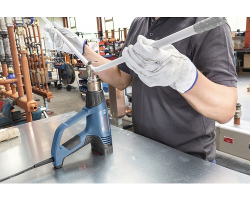 Handwerker biegt mit einer Heißluftpistole ein Kunststoffrohr.