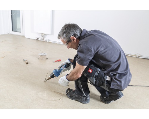 Un artisan soude un sol avec un appareil de soudure.