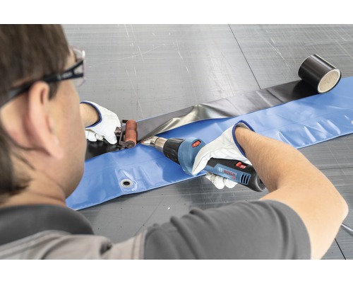 Une personne soude un film avec un pistolet à air chaud et un rouleau de pression.