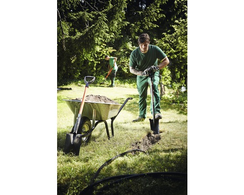 Gartenarbeiter beim Ausheben eines Grabens mit einem Spaten neben einer Schubkarre voller Erde.