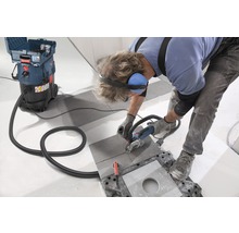 Un artisan coupe un carreau avec une meuleuse d''angle, un aspirateur industriel aspirant la poussière.