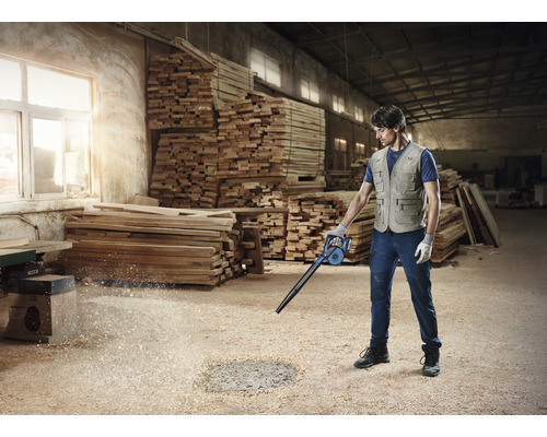 Mann reinigt Werkstatt mit einem Laubbläser von Holzspänen.