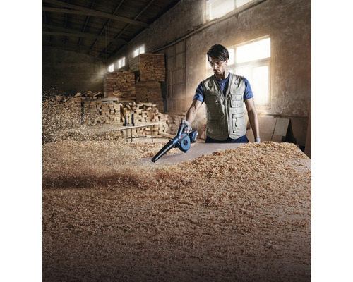 Mann säubert Werkbank mit Laubbläser von Holzspänen