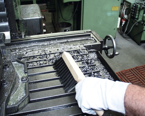 Une personne nettoie un établi avec une brosse pour enlever les copeaux de métal.