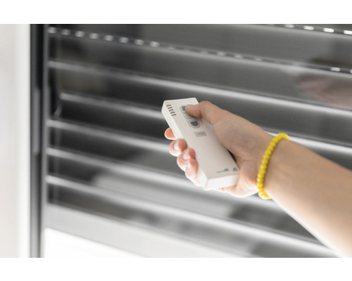 Eine Person bedient mit einer Fernbedienung eine Jalousie.