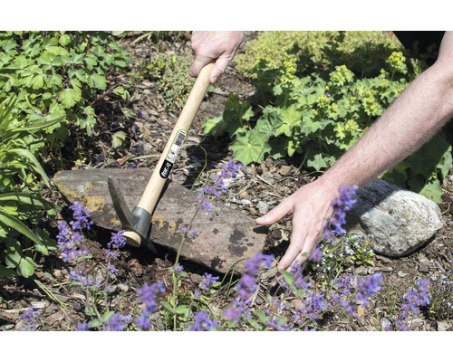 Person arbeitet im Garten mit einer Spitzhacke mit Holzgriff.