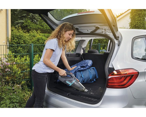Frau saugt Kofferraum mit Akku-Handsauger