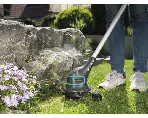 Une personne utilise un coupe-bordures à batterie Gardena dans le jardin.