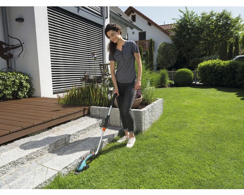 Une femme coupe les bordures de pelouse avec une cisaille à gazon sans fil dans le jardin.