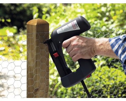 Eine Person befestigt einen Maschendrahtzaun mit einem elektrischen Tacker an einem Holzpfosten.