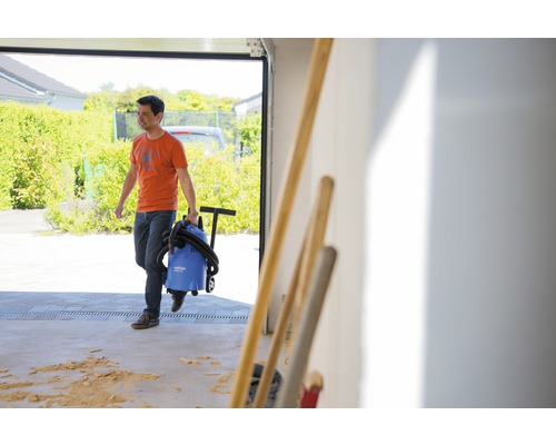 Un homme transporte un aspirateur eau et poussière hors d''un garage.