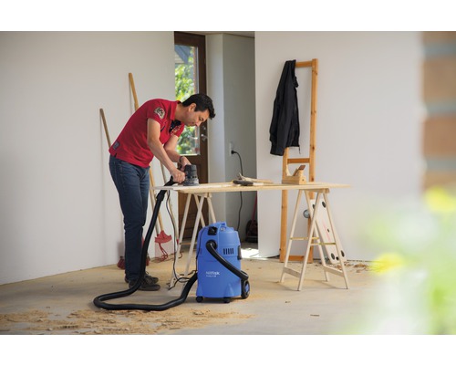 Homme ponçant du bois avec une ponceuse à côté d''un aspirateur dans un atelier