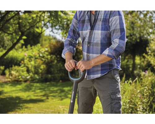 Une personne tient une bêche de la marque Gardena dans un jardin.