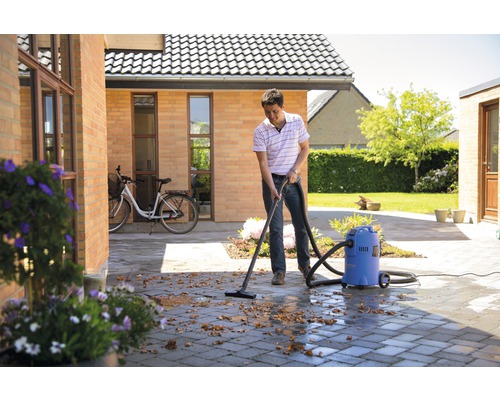 Un homme nettoie une terrasse avec un aspirateur eau et poussière des feuilles.