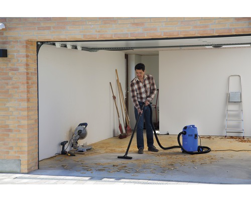Un homme aspire des copeaux dans un garage avec un aspirateur industriel