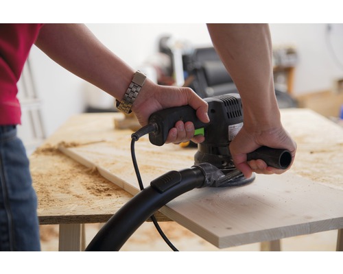 Une personne ponce une planche de bois avec une ponceuse excentrique.