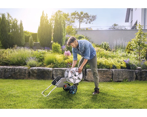 Mann wickelt Gartenschlauch auf Schlauchwagen in Garten auf